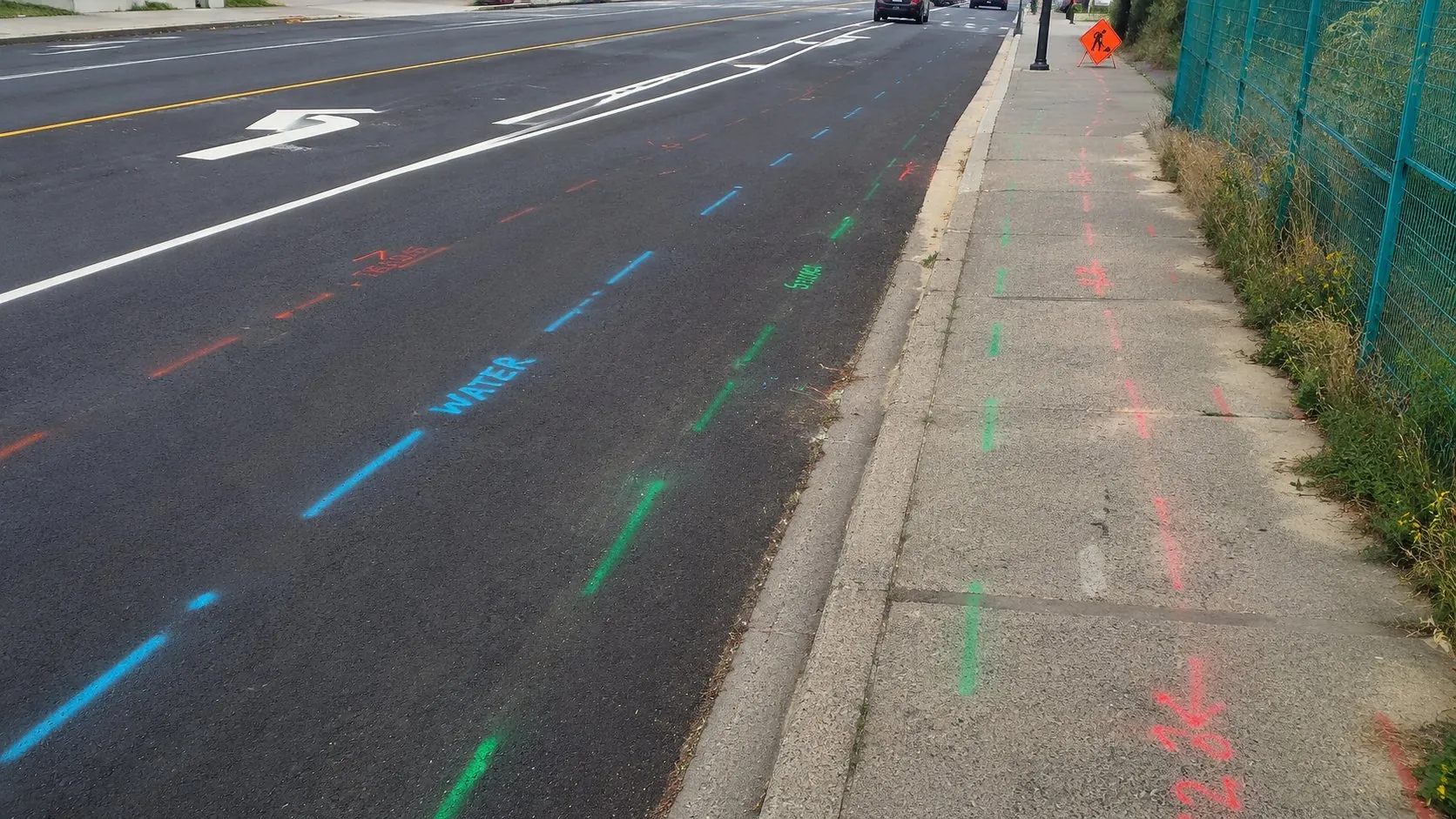 Colour-coded water, sewer, and telecom locate marks along a municipal roadway